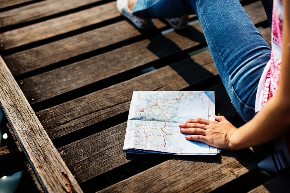 Lista de backpackers Mano de una chica sentada en un muelle de madera encima de un mapa